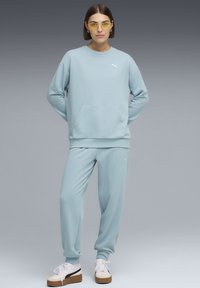 Világoskék pulóver elülső zsebbel és bordázott mandzsettákkal, hozzáillő melegítőnadrággal párosítva. Fehér logó részlet a pulóveren. Kényelmes, laza fazon.