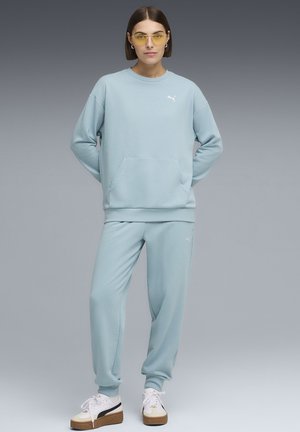 Hellblauer Pullover mit Fronttasche und gerippten Bündchen, kombiniert mit passenden Jogginghosen. Weißes Logo-Detail auf dem Pullover. Legere Passform.