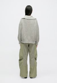 Hall hallitatud kampsun laia kraega, kombineeritud lahtiste oliivroheliste tegevusteks mõeldud pükstega, millel on suured taskud ja kahe tekstuuriga disain.