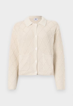Cream knitted cardigan featuring a diamond pattern, collared neckline, button closure, and two front pockets. Textured fabric.