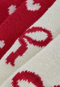Wełniany dzianinowy materiał w kolorze czerwonym i białym, z wzorami w kształcie serc i okręgów, z teksturowanymi detalami i kontrastującymi kolorami w układzie w paski.