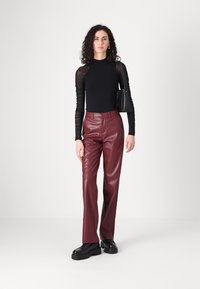Haut noir à manches longues avec des manches transparentes froncées, associé à un pantalon en simili cuir bordeaux taille haute et des chaussures compensées noires.