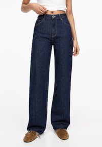 High-waisted, dark blue wide-leg jeans with a zipper fly, orange stitching, and front pockets. The fabric has a smooth texture.
