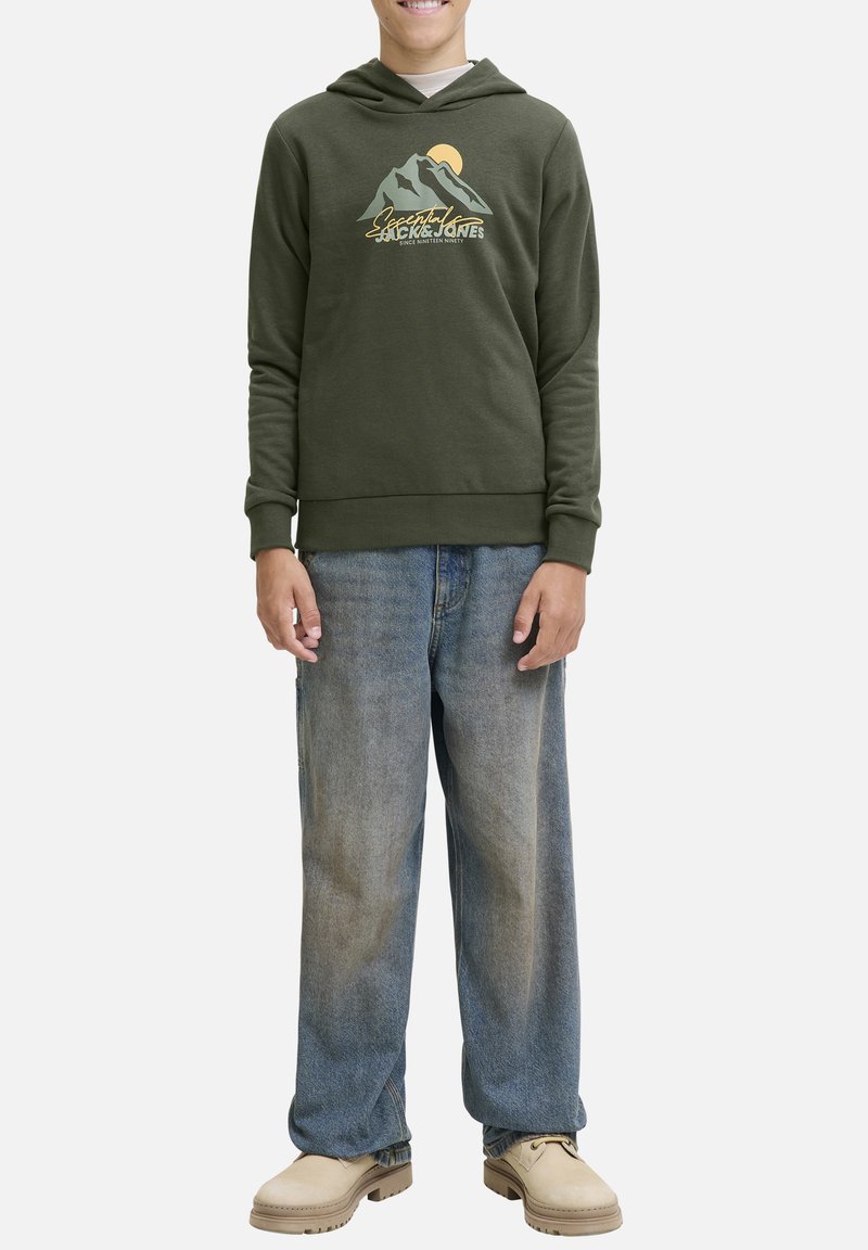 Olijfgroene hoodie met een grafisch ontwerp van een berg en de zon, gecombineerd met losse blauwe jeans. Het model staat op een neutrale achtergrond en toont de outfit.