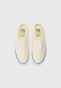 Canvas sneakers in light yellow with white laces, blue logo, and blue outsole trim. Classic low-top design with round toe.