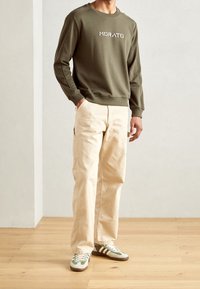 Kaki grön sweatshirt med broderad "MORATO", krämfärgade vida byxor och gröna Adidas-sneakers med vita ränder och texturerat tyg.