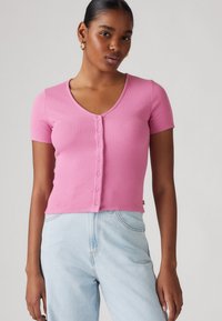 Top rose ajusté à manches courtes avec un décolleté en V et six boutons sur le devant. Assorti à un jean en denim bleu clair.