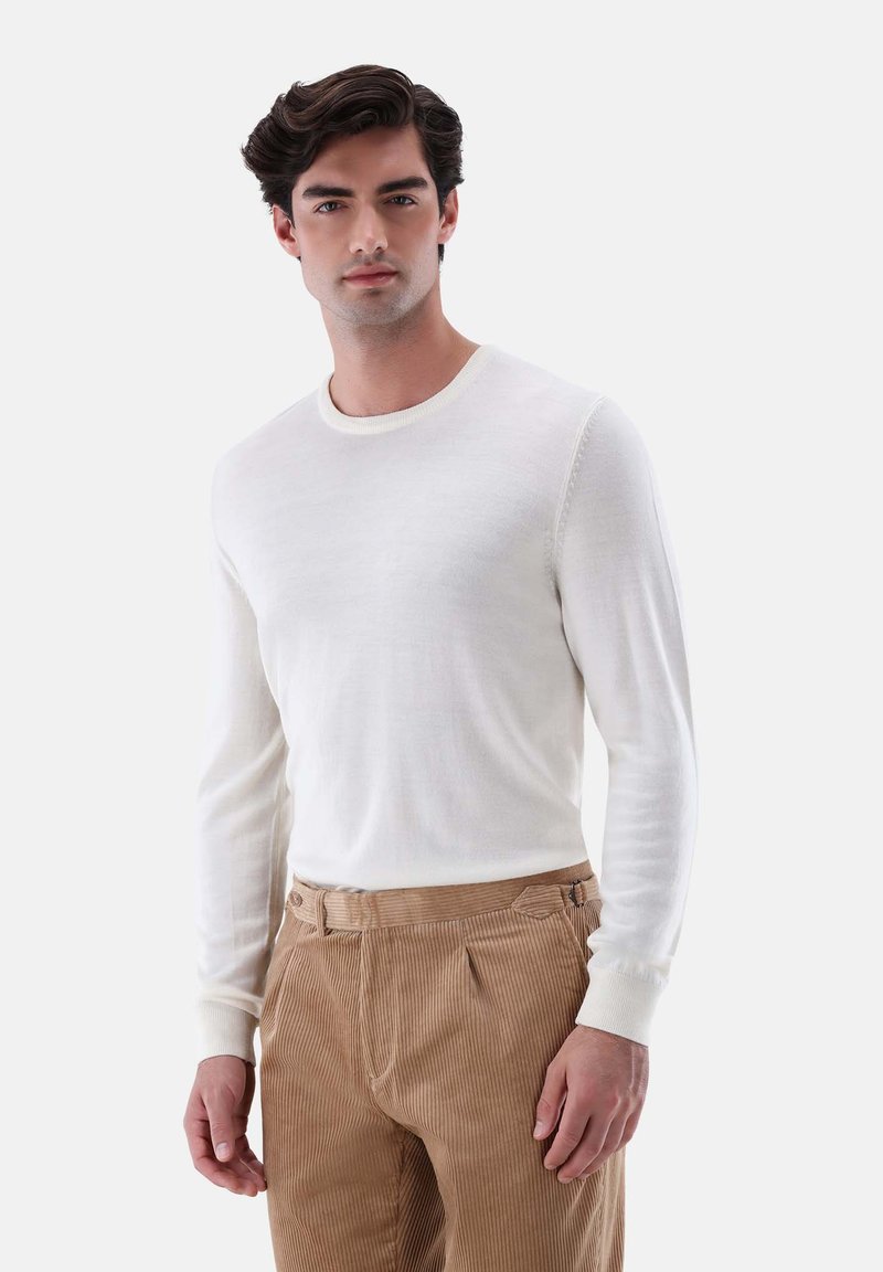 Weißer Langarmpullover aus leichtem Stoff mit Rundhalsausschnitt, kombiniert mit hellbraunen Cordhosen mit seitlichen Taschen und strukturierten Streifen.