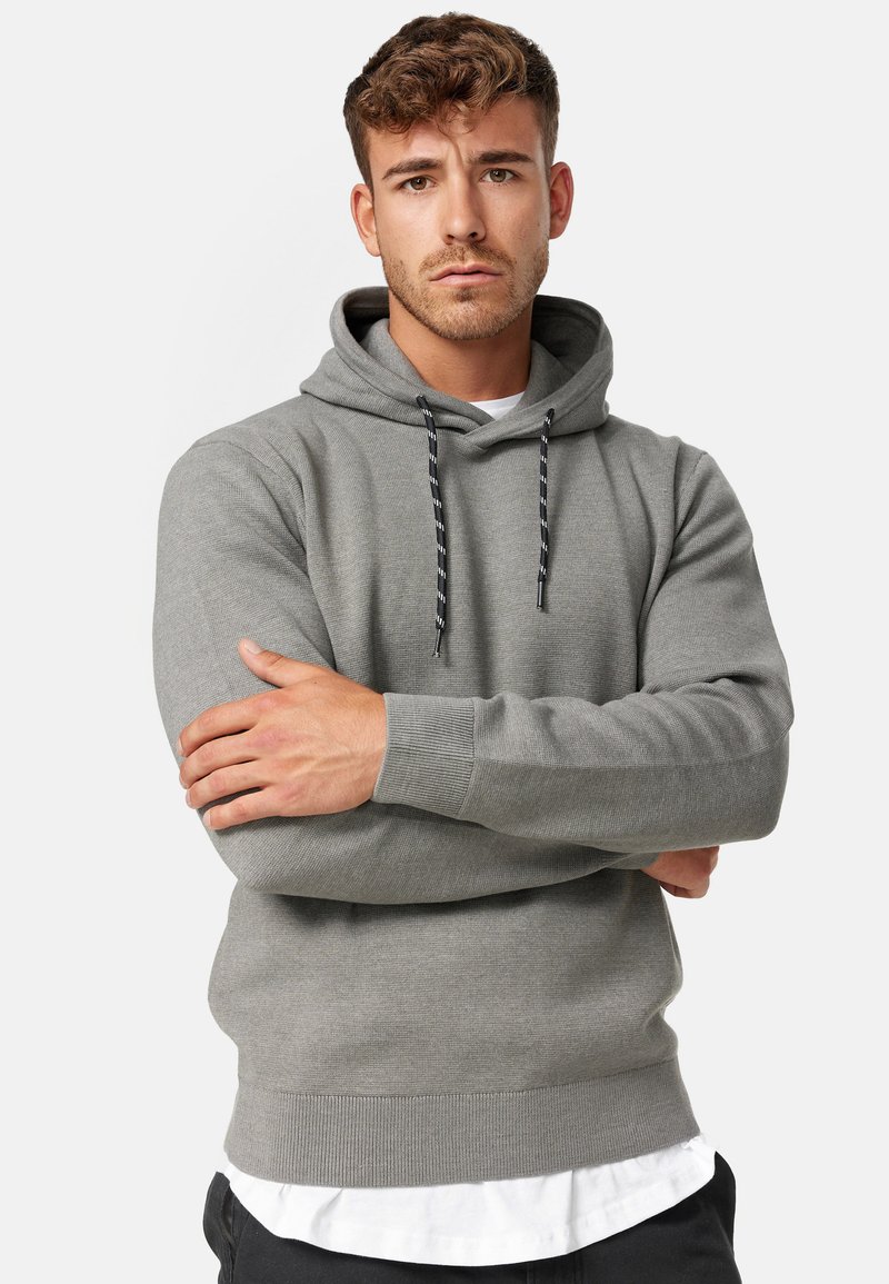Grijze hoodie met een gestructureerde afwerking, voorzien van een trekkoordkap, geribbelde manchetten en zoom, gedragen over een wit shirt.