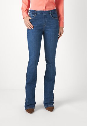 Jeans de mezclilla azul oscuro con pierna acampanada, cinco bolsillos y costuras decorativas cerca de la cintura, combinados con zapatos de tacón alto marrones.