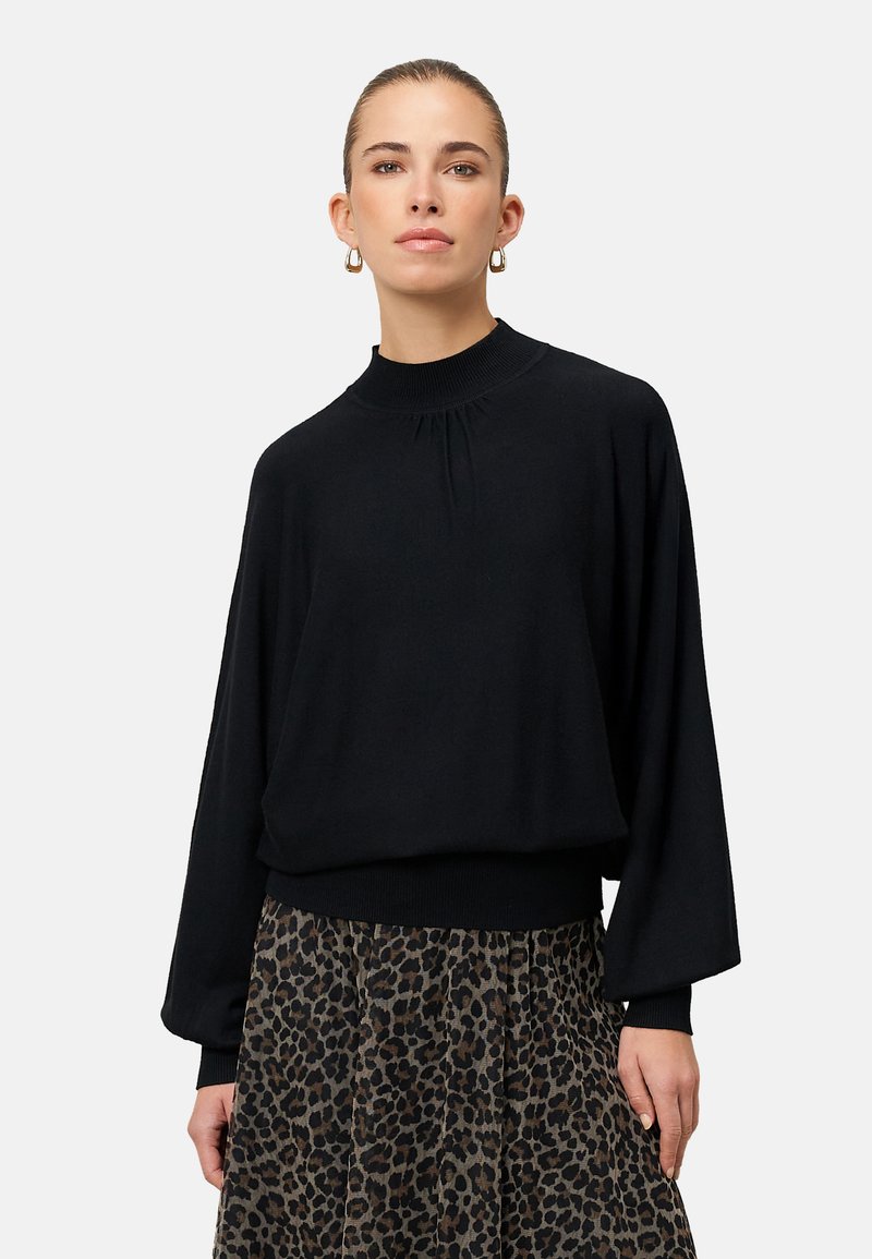Czarny sweter z długim rękawem, wysokim dekoltem i marszczonym detalem, zestawiony z spódnicą w lamparta. Miękka tkanina, luźny fason, prążkowane akcenty.