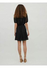 Zwart jurkje met korte pofmouwen, textuurstof, een taille met een strik en een uitlopende rok, met een strikdetail aan de achterkant. Gecombineerd met beige hakken.