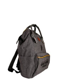 Gray fabric backpack with a roll-top design, leather accent, gold zipper, front pocket, and printed branding on the lower section.