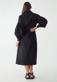 Schwarzes, langärmliges Kleid mit tailliertem Bund, übergroßen Puffärmeln und Kragen. Glatte Textur und minimalistisches Design.