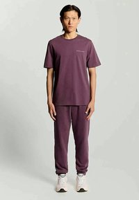 Conjunto combinado em roxo escuro, composto por uma t-shirt de mangas curtas e calças de jogger, feito de um tecido suave, com uma marcação mínima no peito.