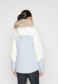 Helles, blaues, wasserdichtes Jacket mit einem weißen Oberteil und einer mit Fell besetzten Kapuze, das durch ein straffes Design und subtile Nahtdetails besticht.