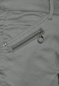 Närbild av en grå byxficka med diagonalt blixtlås och rund metalldragare.