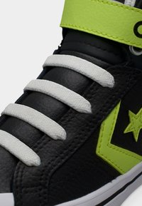 Μαύρο δερμάτινο αθλητικό παπούτσι με λευκά κορδόνια, φουσκαλίζουσα φορεσιά σε νεον πράσινο χρώμα, λογότυπο αστέρι και λευκή σόλα σε κοντινή λήψη.