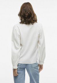 Hvid, langærmet bluse med struktureret stof, rundet kant og knapdetaljer ved manchetterne. Stylet med lyseblå jeans.