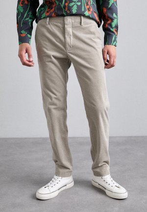 Beige Cordhosen mit strukturiertem Finish, Slim-Fit-Design und seitlichen Taschen; kombiniert mit weißen Sneakern.