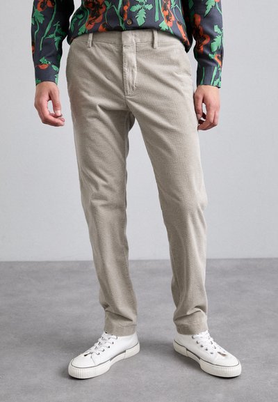 Pantalons en velours côtelé beige avec une finition texturée, coupe slim, et poches latérales ; associés à des baskets blanches.