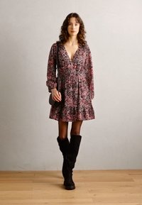 Floral-patterned, pink and black dress with a V-neck, long sleeves, and a flared skirt. Black knee-high boots; small black handbag.