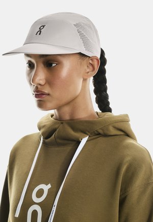 Lys grå kasket med en buet skygge, åndbare mesh-sidenheder og et sort logo. Olivengrøn hoodie med hvide snore og markante logo-detaljer.