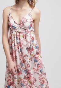 Robe maxi fleurie avec des bretelles spaghetti, présentant une base blanche, un motif floral rose et bleu, et un corsage ajusté avec une jupe fluide.