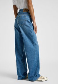 Vaqueros de pierna ancha en azul claro con una cintura alta, que presentan una etiqueta de cuero marrón y bolsillos traseros tradicionales, fabricados en tela de denim.