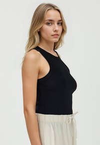Top nero senza maniche con scollatura tonda, realizzato in tessuto morbido, abbinato a pantaloni beige chiaro con cordoncino. La silhouette è aderente.