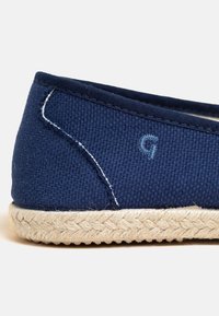 Marinefarbene Canvas-Slipper mit gewebter Jutesohle. Verfügt über gestickte Akzente und ein kleines gesticktes Buchstaben 'G' in passendem Blau.