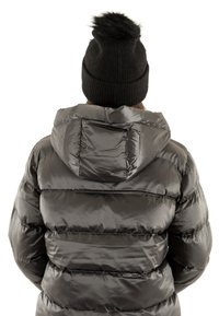 Giacca a vento nera con cappuccio, caratterizzata da una superficie lucida e trapuntata. Il modello indossa un berretto nero a maglia decorato con un pompon in pelliccia sintetica.