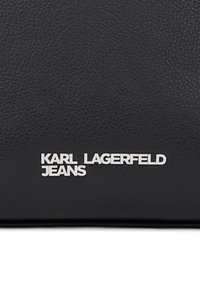 Čierny textúrovaný kožený povrch s strieborným kovovým nápisom "KARL LAGERFELD JEANS" v dolnej časti na strede.