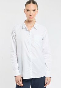 Chemise blanche à manches longues avec une poche poitrine simple, en tissu lisse, présentant un col classique et une fermeture à boutons.