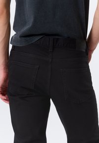 Black denim jeans with a straight cut, featuring back pockets and a branded waistband. The fabric has a smooth, dark finish.