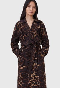 Cappotto trench leopardato in marrone e nero. Presenta una vita con cintura, ampi revers e due tasche frontali con dettagli a bottone.