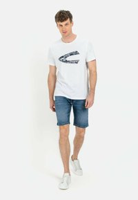 Hvid bomulds t-shirt med et navy grafisk design, parret med blå denim shorts og hvide sneakers. Enkel, afslappet herretøj.