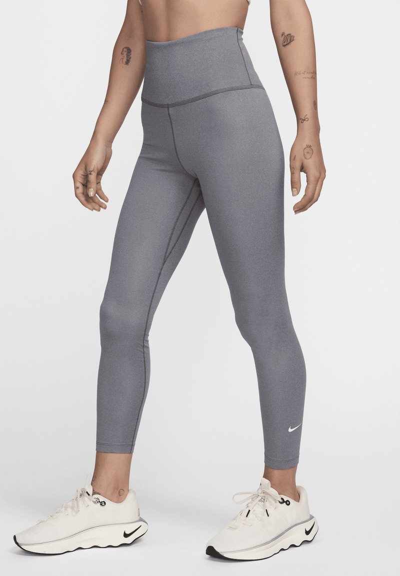 Sive visokotalasne tajice sa glatkom teksturom, koje imaju kontrastne šavove i mali Nike logo na donjem delu noge.