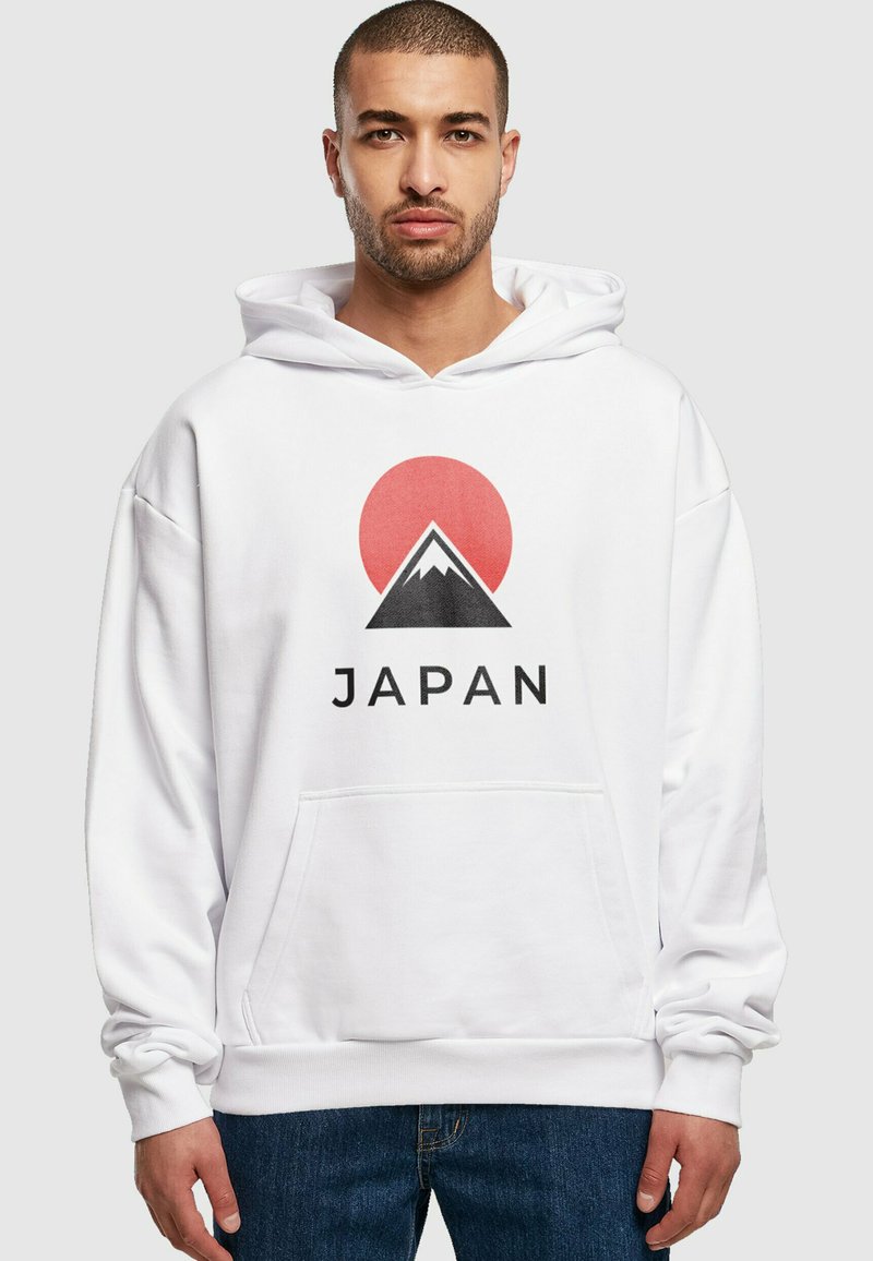 Fehér kapucnis pulóver, nagy hegymászás és piros nap grafika található rajta, az "JAPÁN" szó feketén a design alatt. Puha tapintású, laza fit.