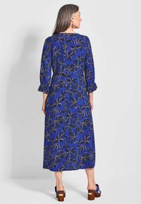 Blaues Blumenkleid mit Dreiviertelärmeln, gerafften Manschetten und einem langen, fließenden Design. Hergestellt aus leichtem Stoff mit einem Blattmuster.