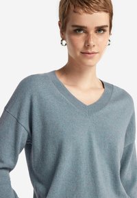 Jasnoniebieski sweter dzianinowy z dekoltem w kształcie V, opuszczonymi ramionami i długimi rękawami. Miękka tekstura i lekko luźny krój.