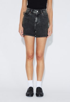 Sorte denimshorts med høj talje, frynset kant og kontrastsyning. Kombineret med sorte loafers og hvide ankelstrømper.