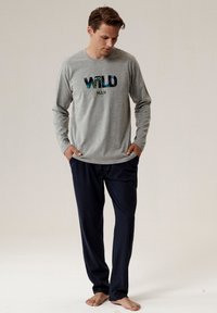 Szara koszula z długim rękawem z grafiką "WILD MAN", połączona z granatowymi spodniami. Miękka tkanina, luźny krój i minimalistyczny design.