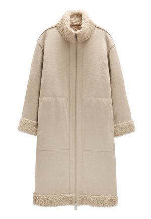 Beżowy płaszcz z wysokim kołnierzem i zamkiem błyskawicznym z przodu. Miękkie, teksturowane akcenty z baraniej wełny na kołnierzu i rękawach. Dwie duże kieszenie z przodu.