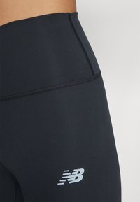 Leggings noirs à taille haute en tissu lisse et extensible. Présentent un petit logo blanc contrastant de New Balance sur le bas de la jambe.