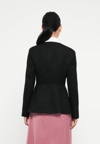 Zwarte peplum-jack met een gestructureerde stof, lange mouwen en een getailleerde pasvorm, gecombineerd met een zachtroze rok. Eenvoudig witte kraagdetail.
