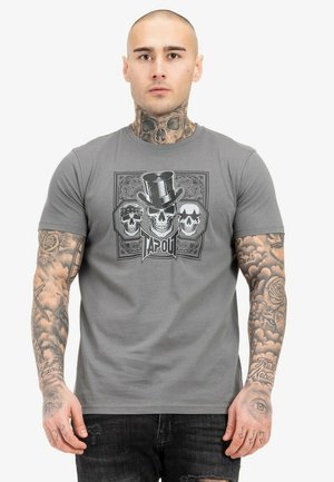 Graues T-Shirt mit einem grafischen Design von drei Schädeln, einer davon mit einem Zylinder, und dem Markennamen "TAPOUT" darunter. Aus Baumwolle, mit kurzen Ärmeln.