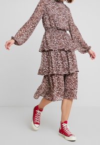 Vícevrstv dress midi z lehké, vzorované látky v odstínech hnědé, červené a krémové, doplněné červenými vysokými teniskami.