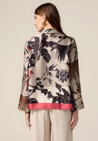 Blusa di seta con motivo floreale e foglioso in nero, rosso e beige, con maniche ampie e un orlo in satin rosa nella parte inferiore.