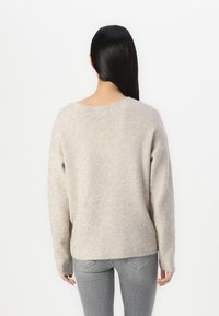 Helles beige Sweatshirt mit gerippter Textur, abfallenden Schulternähten und lockerer Passform. Hat einen runden Ausschnitt und lange Ärmel.